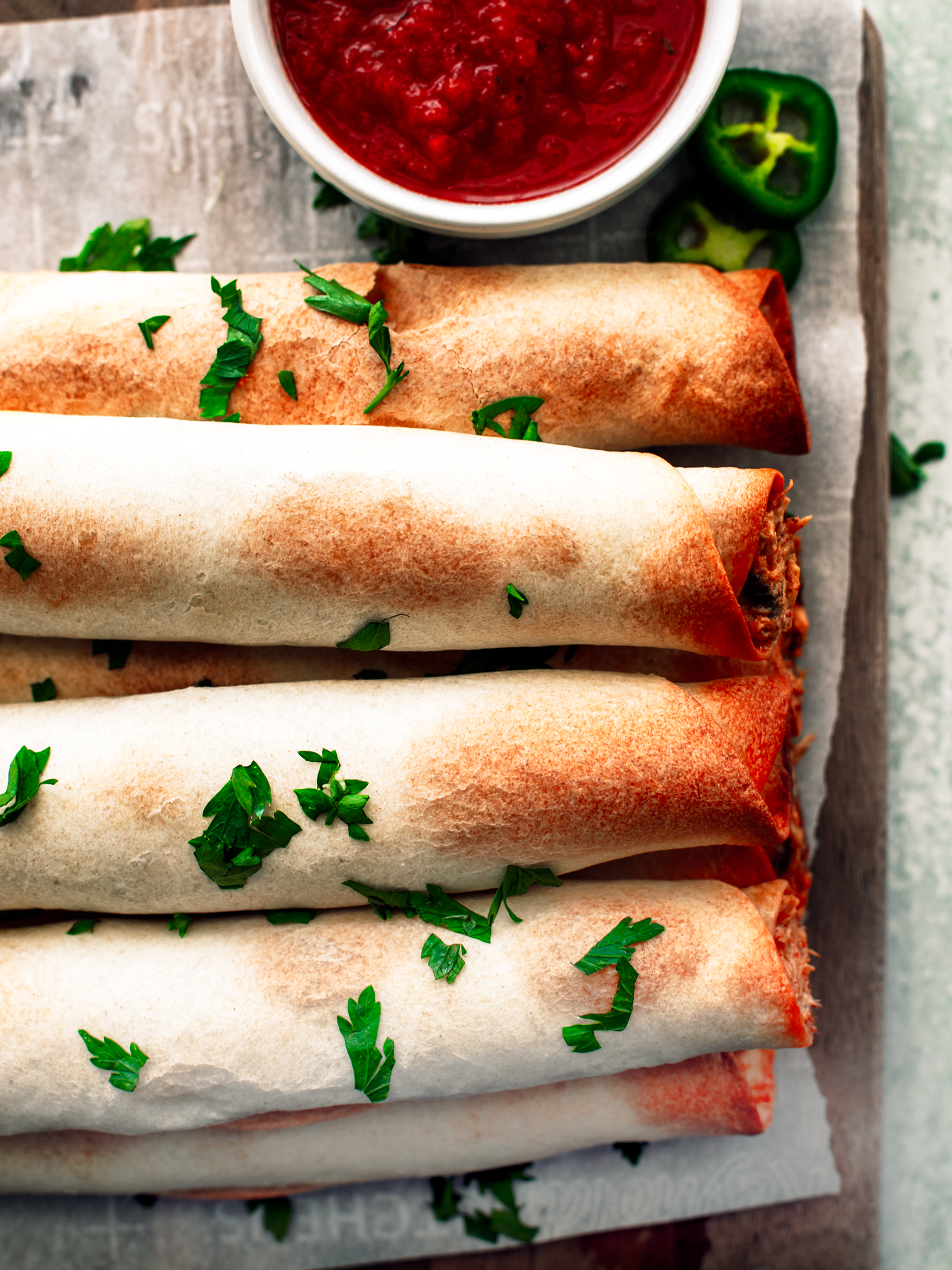 Close up of baked flautas on parchment-covered serving board.