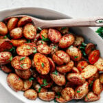 Roasted mini potatoes in a serving dish with a wooden spoon.