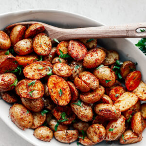 Roasted mini potatoes in a serving dish with a wooden spoon.