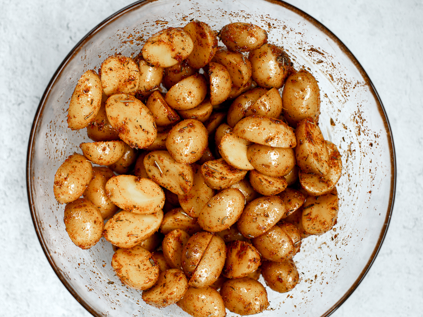 Oiled and seasoned small potatoes in a mixing bowl.