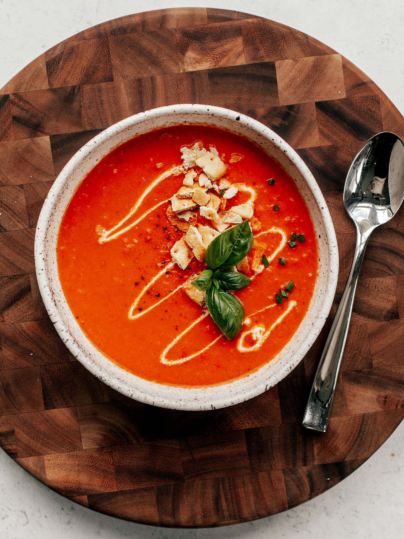 Bowl of tomato soup with cream drizzle, crushed crackers, and basil leaves.