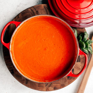Big pot of tomato soup on a wooden cutting board.