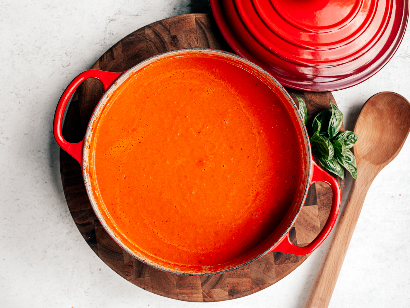 Big pot of tomato soup on a wooden cutting board.