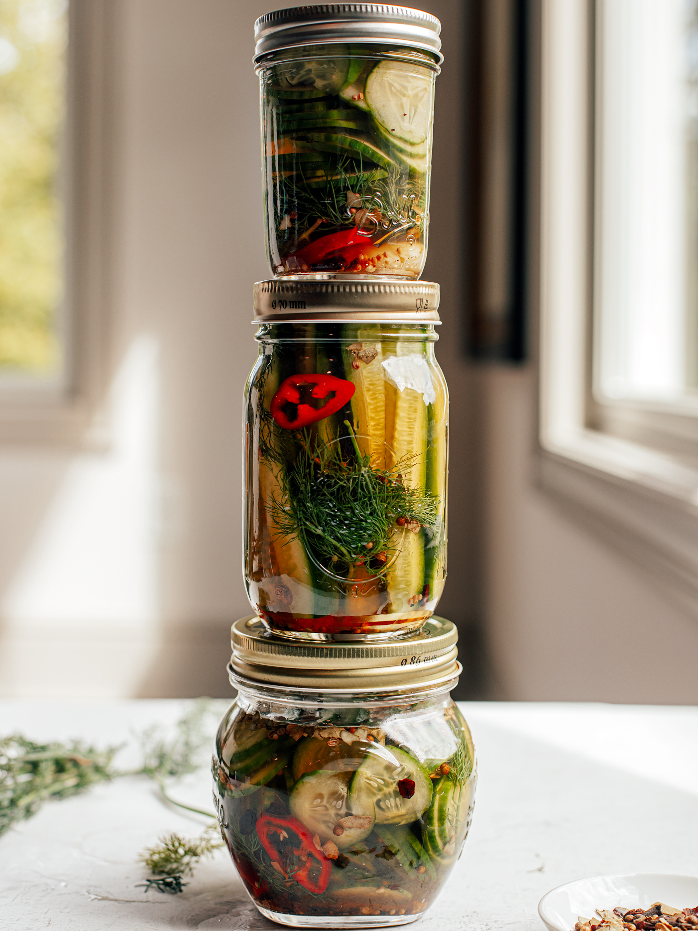 Three different sized jars of refrigerator pickles stacked on top of one another on a countertop.