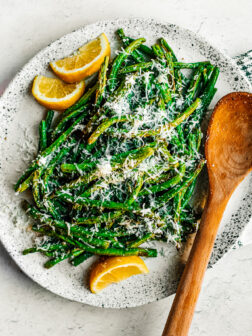 Green beans on a white serving plate with lemon wedges.