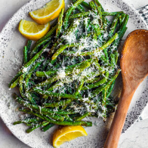 Serving plate of green beans with lemon wedges and grated parmesan.