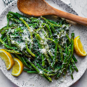 Serving plate of green beans with lemon wedges and grated parmesan.