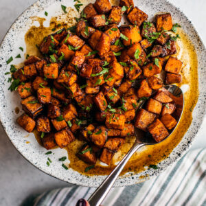 Serving plate of cubed sweet potatoes in honey lime sauce with serving spoon.
