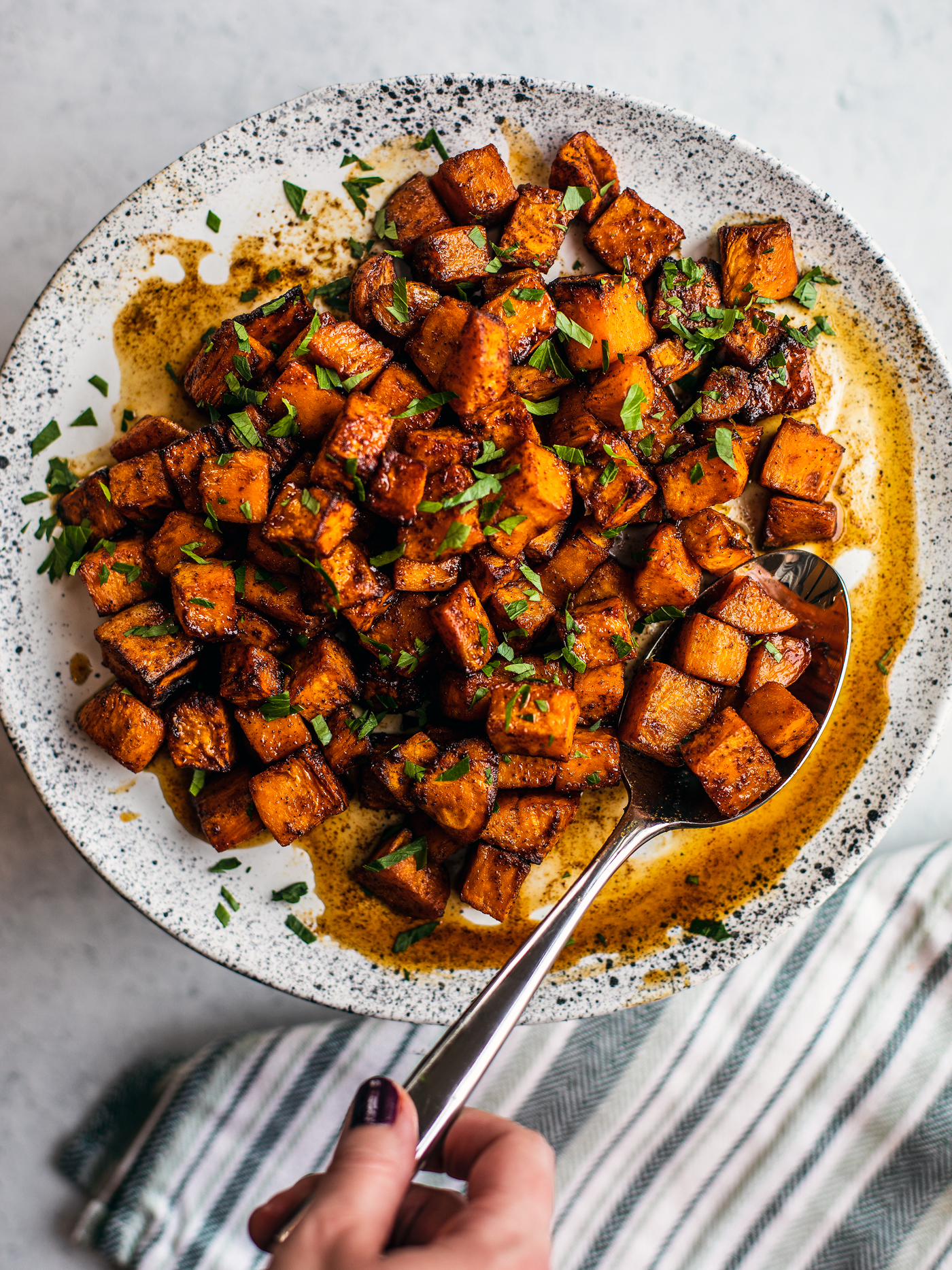 Serving plate of cubed sweet potatoes in honey lime sauce with serving spoon.