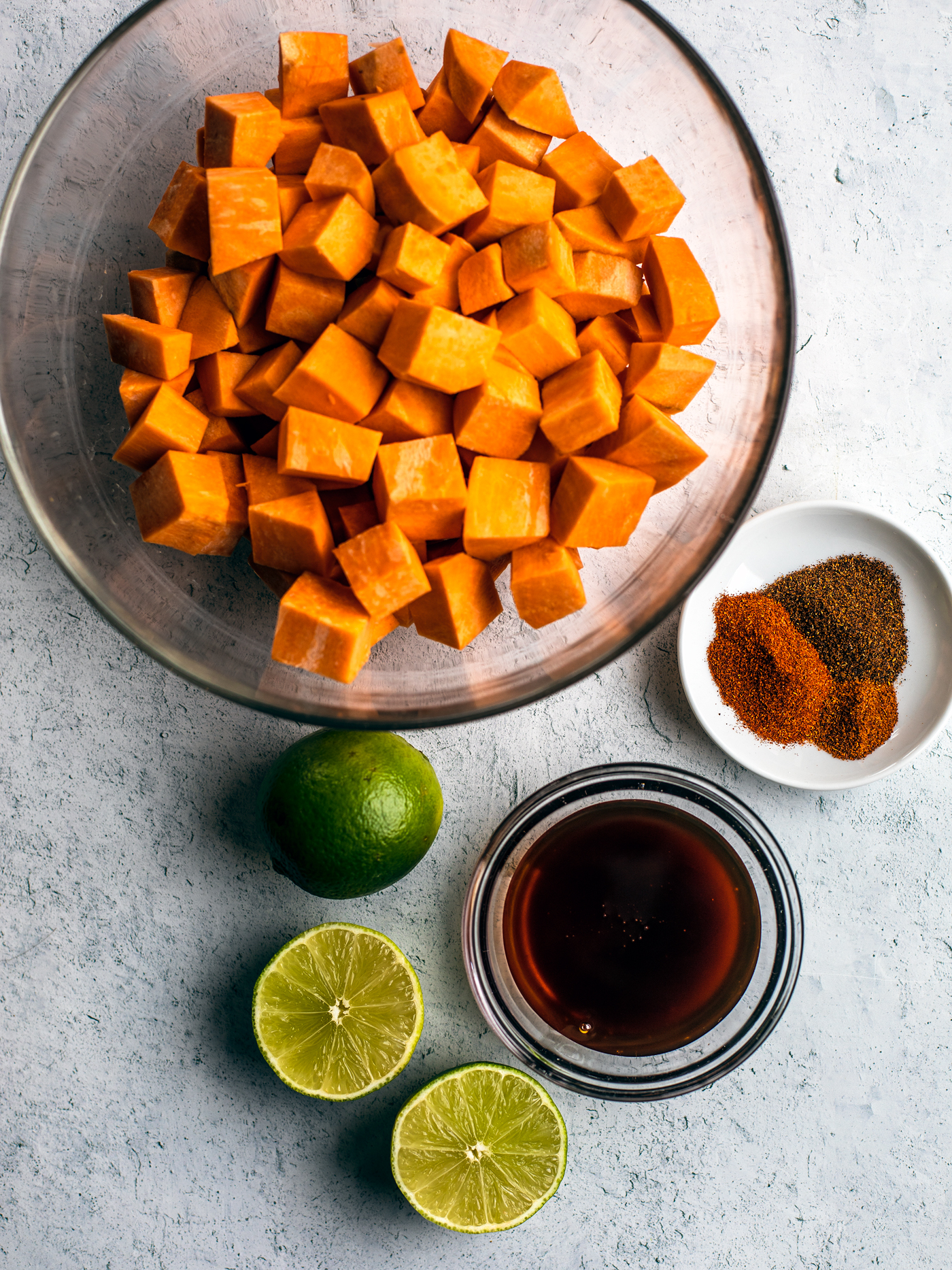 Bowl of cubed sweet potatoes, bowl of honey, pinch bowl of spice blend, and limes.