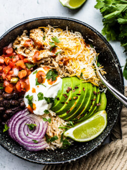 Black bowl filled with rice, pico de gallo, black beans, onions, avocado, and shredded chicken.