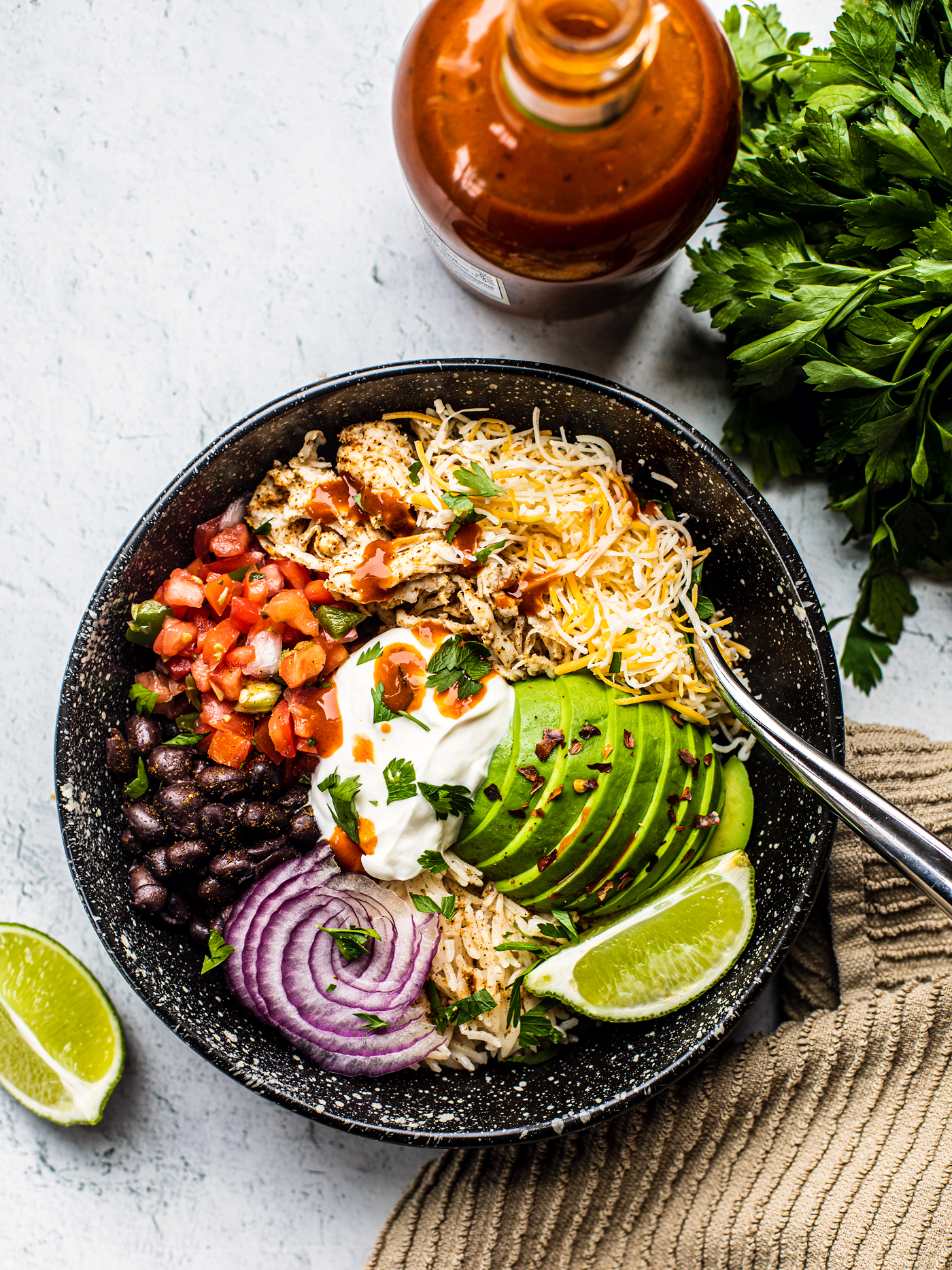 Black bowl filled with rice, pico de gallo, black beans, onions, avocado, and shredded chicken.