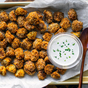 Baking sheet full of breaded fried mushrooms with a small bowl of ranch dip.