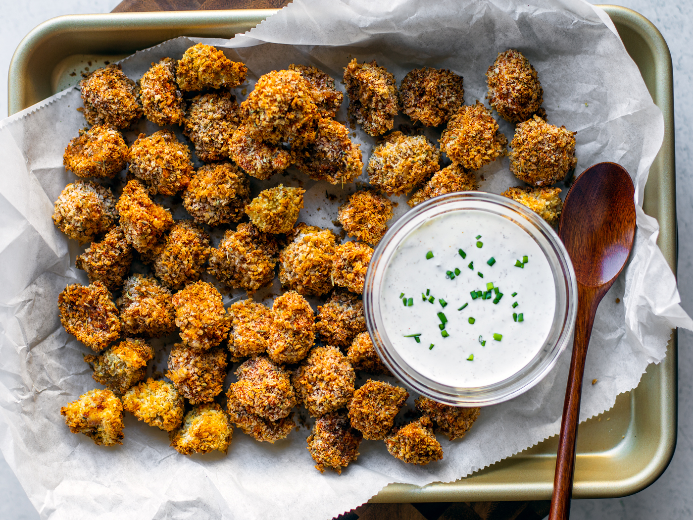 Baking sheet full of breaded fried mushrooms with a small bowl of ranch dip.