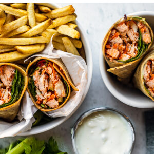 Buffalo chicken halves set in a bowl with fries and another set in a bowl alone with blue cheese on the side for dipping.