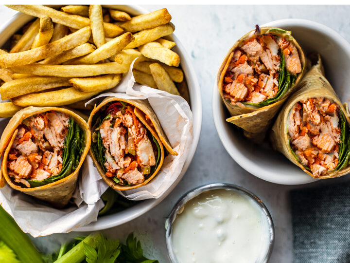 Buffalo chicken halves set in a bowl with fries and another set in a bowl alone with blue cheese on the side for dipping.