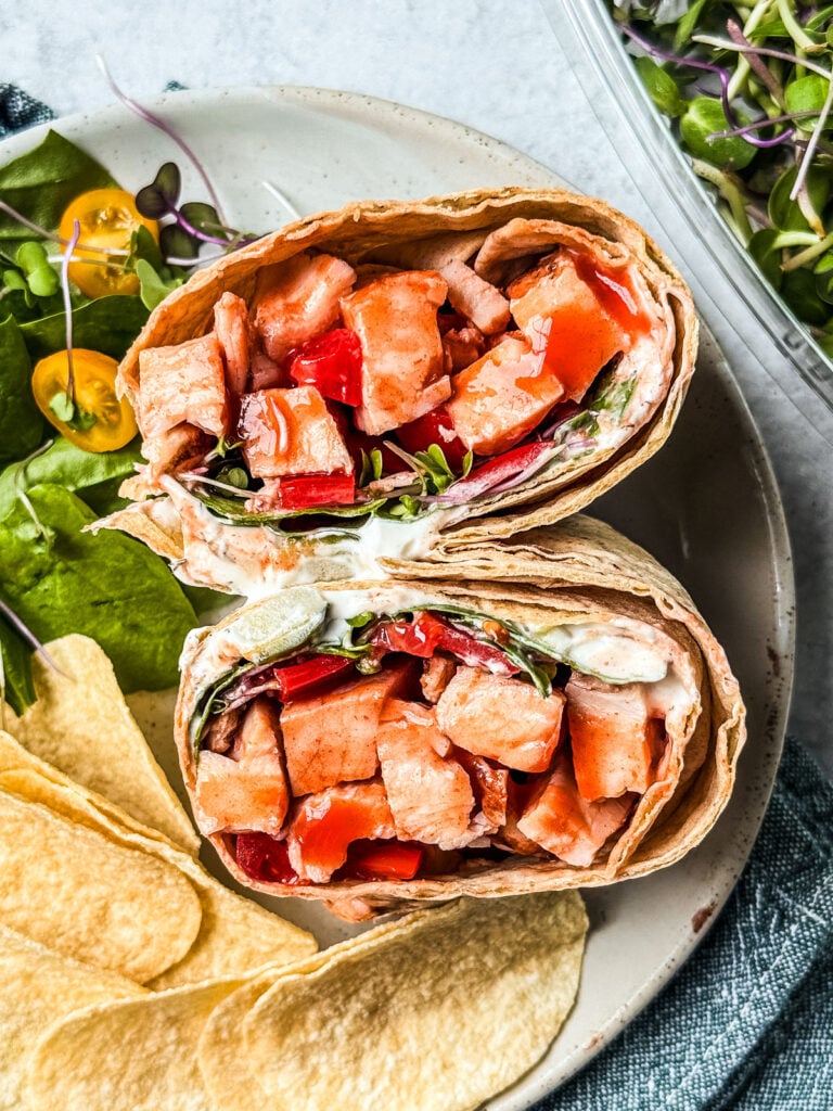 Buffalo chicken wrap on a plate with salad and chips.