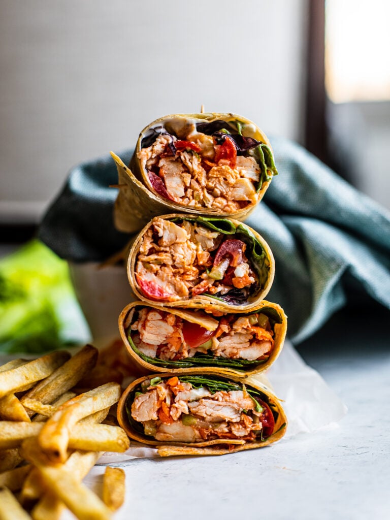 Buffalo wrap halves stacked on top of one another with a side if fries.