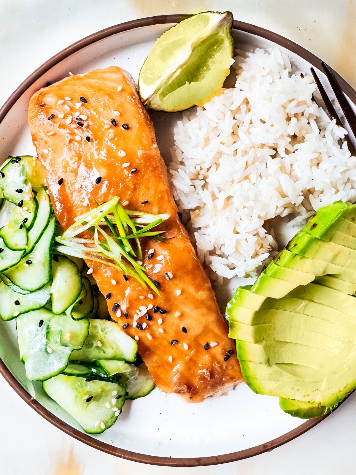 Baked miso salmon on a plate with rice, avocado, and cucumber salad.