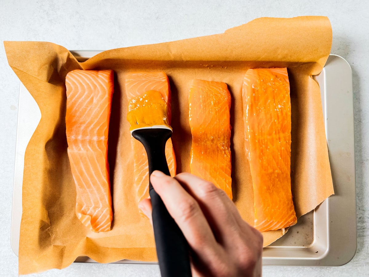Fillets of salmon on a baking sheet being brushed with miso glaze.