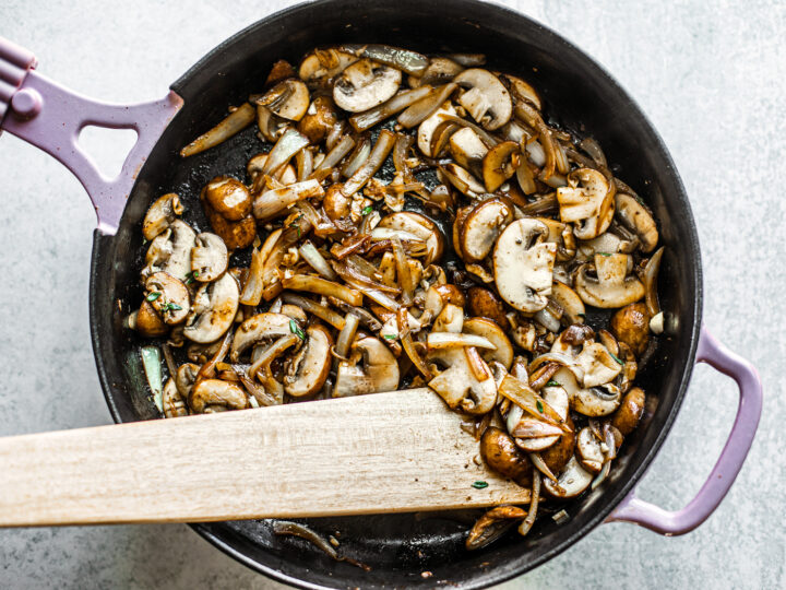 Mushrooms and onions being stirred in a skillet.