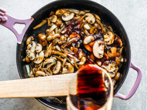 Red wine being poured into skillet with mushrooms and onions.
