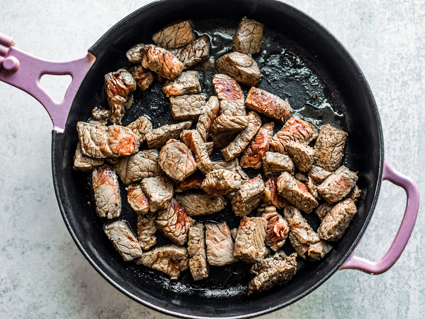 Chunks of medium-rare cooked beef in a skillet.