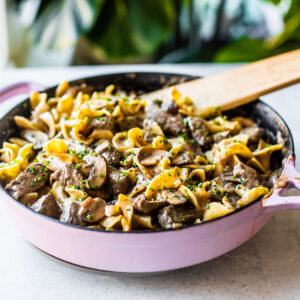 Purple skillet full of beef stroganoff and egg noodles, garnished with chives.