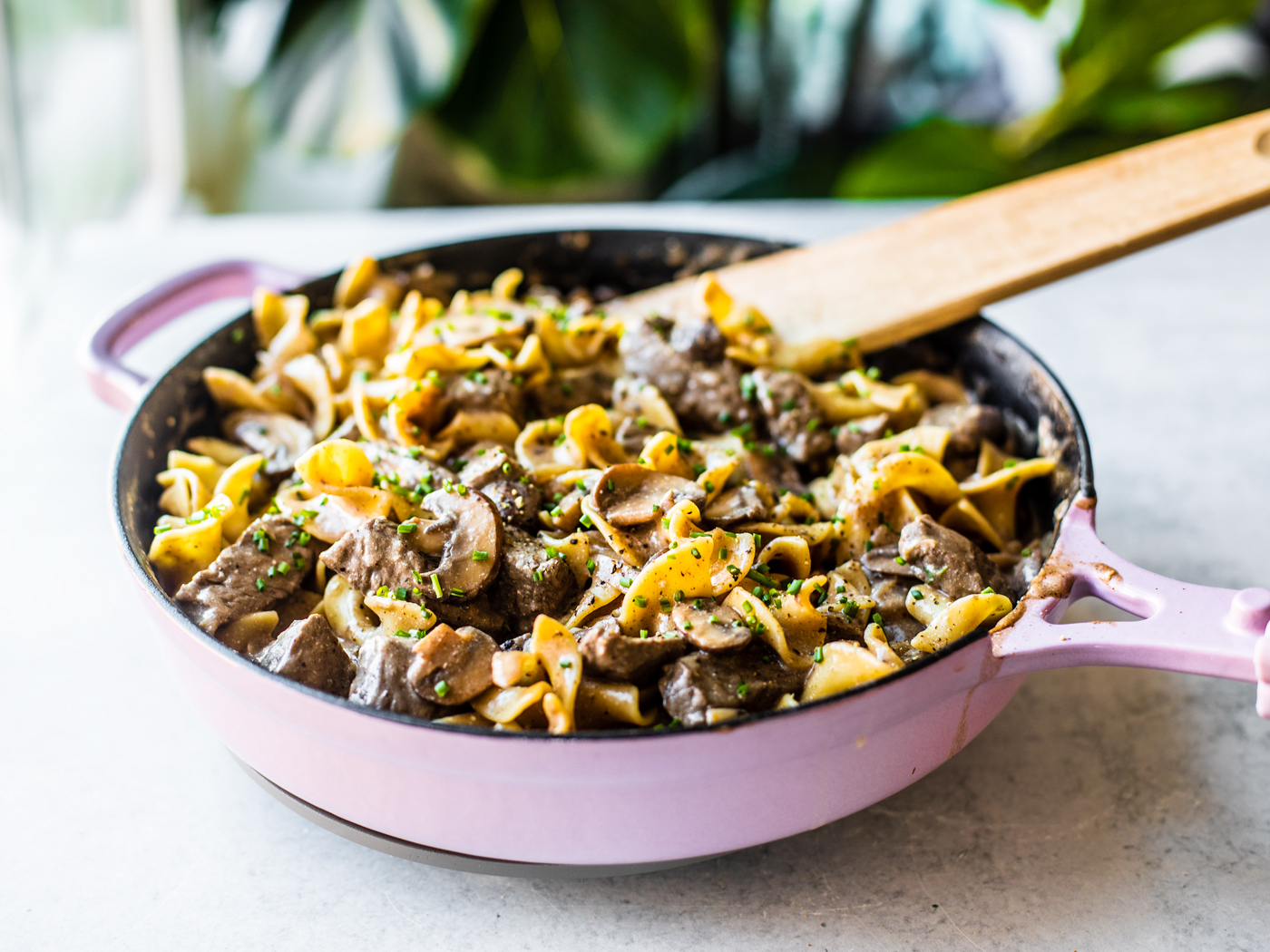 Purple skillet full of beef stroganoff and egg noodles, garnished with chives.