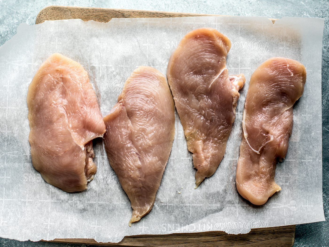 Butterflied chicken breasts on parchment-lined cutting board.