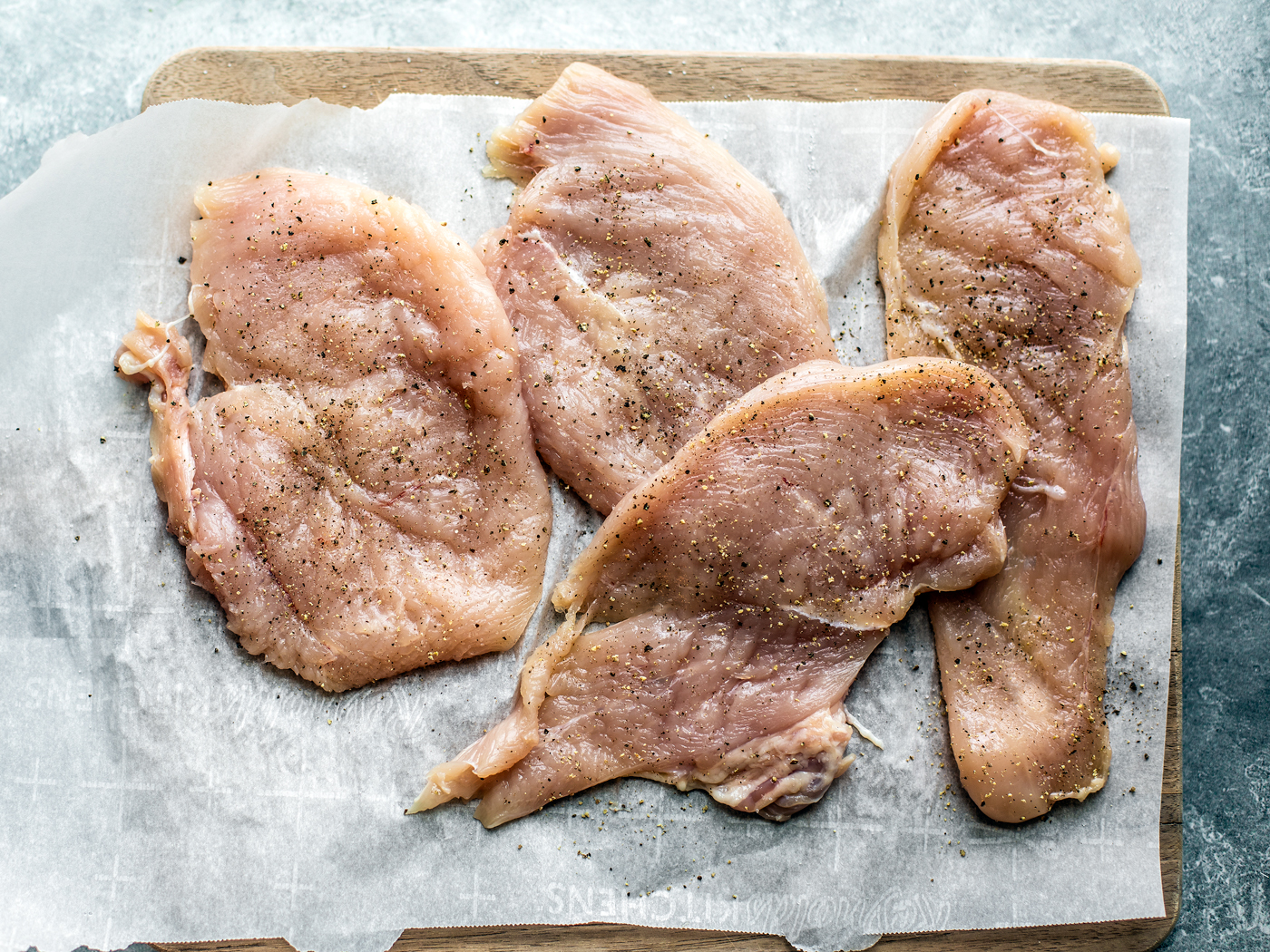 Pounded out chicken cutlets on parchment-lined cutting board.