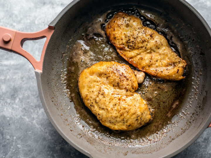 Two golden chicken cutlets in a skillet.
