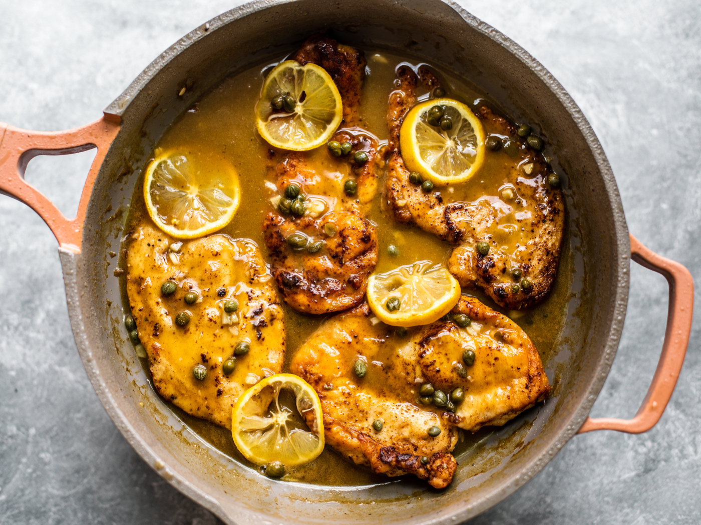 Golden chicken cutlets in skillet with sauce, capers, and lemon slices.