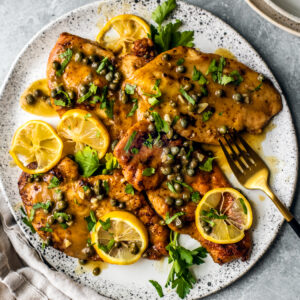 Platter of chicken piccata smothered in sauce, capers, lemon slices, and fresh parsley.