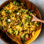 Large bamboo bowl full of colorful couscous salad with bamboo serving spoons.