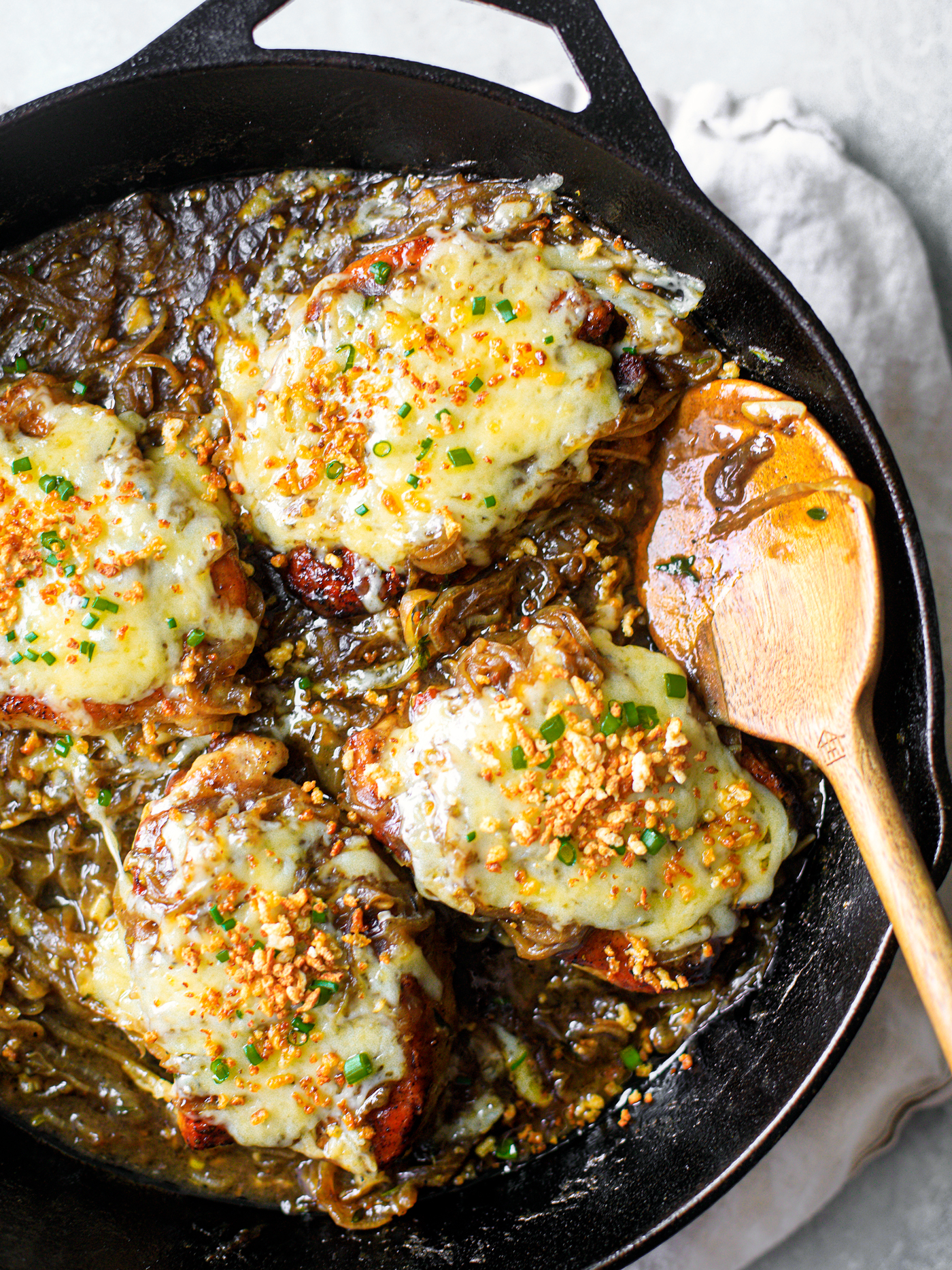 Cheesy pork chops smothered in onion gravy and topped with chives in a cast iron skillet.