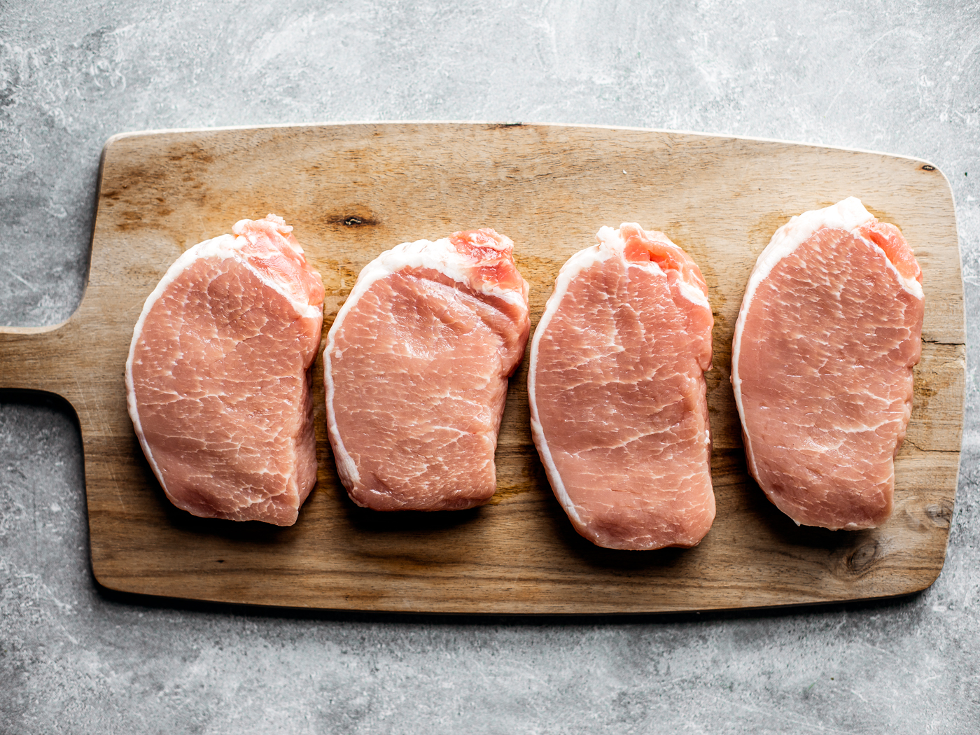Four pork chops lined up on a cutting board.