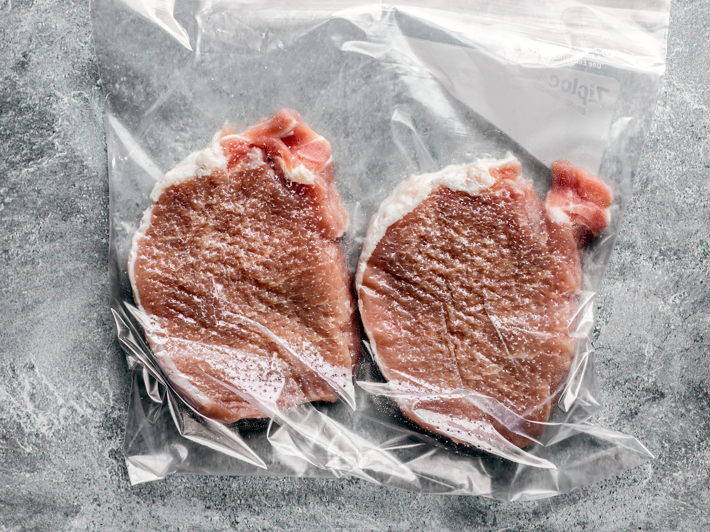 Two pork chops in a freezer bag that have been tenderized.