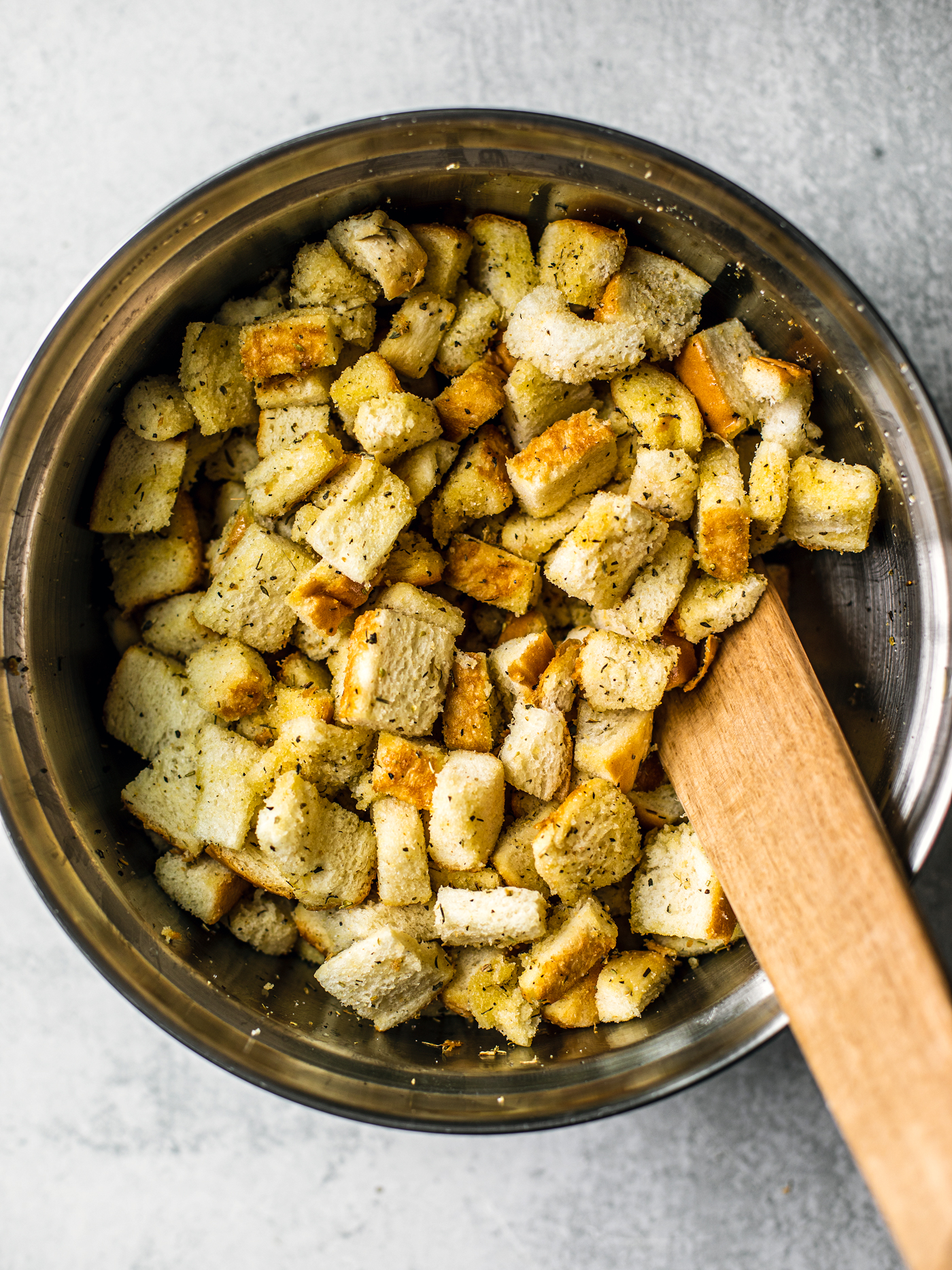 Mixing bowl full of seasoned croutons with a spatula.