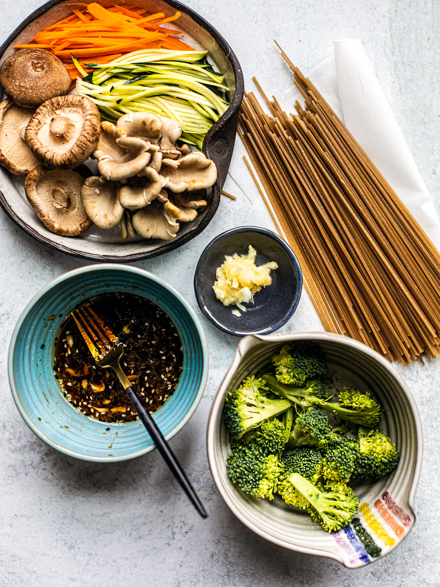 Flatlay shot of uncooked soba noodles, vegetables, and sauce in a mixing bowl.