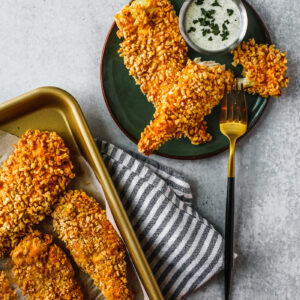Green plate with chicken tenders and ranch dip on it next to a sheet pan of chicken tenders.