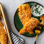 Green plate with chicken tenders and ranch dip on it next to a sheet pan of chicken tenders.