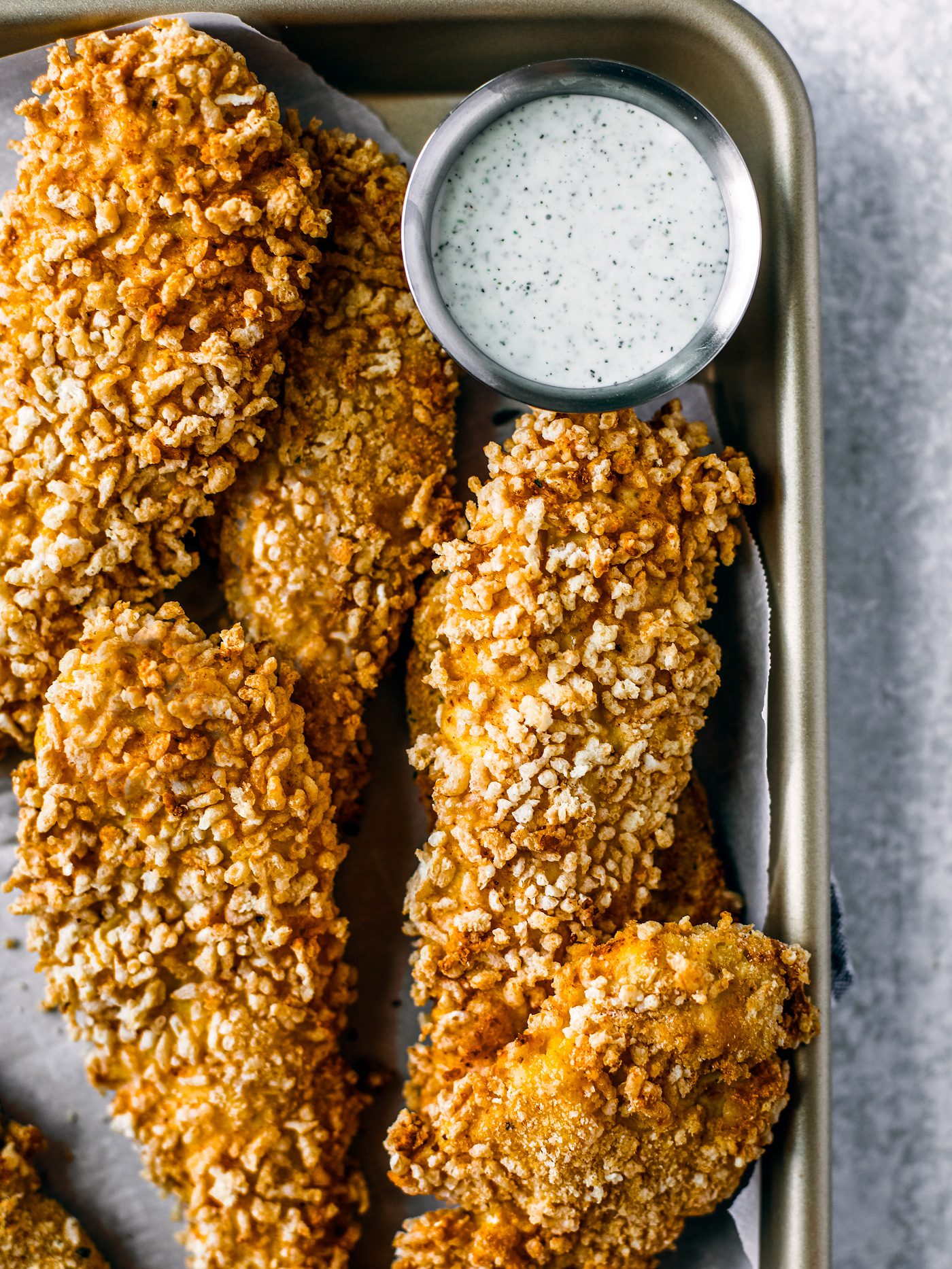 Crispy chicken tenders on a sheet pan with small dipping bowl of ranch.