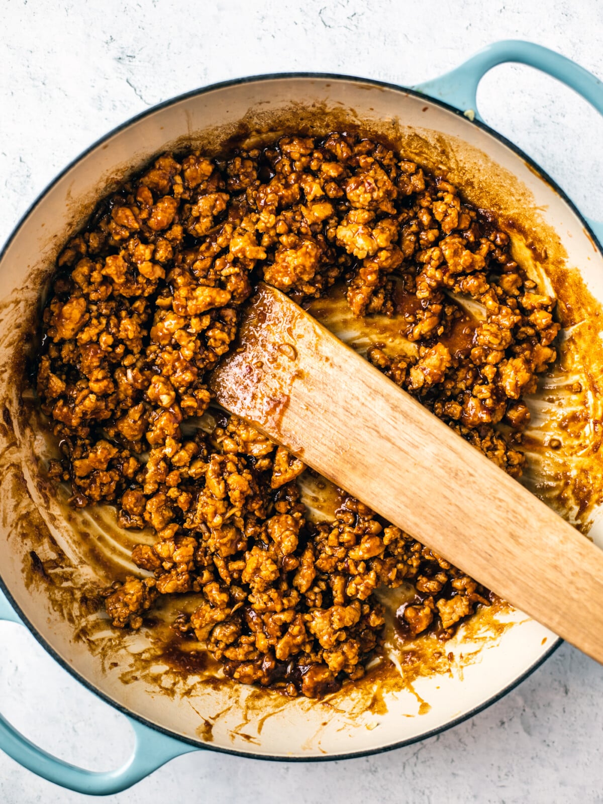 Braiser full of cooked hoisin sesame ground chicken with a wooden spatula.