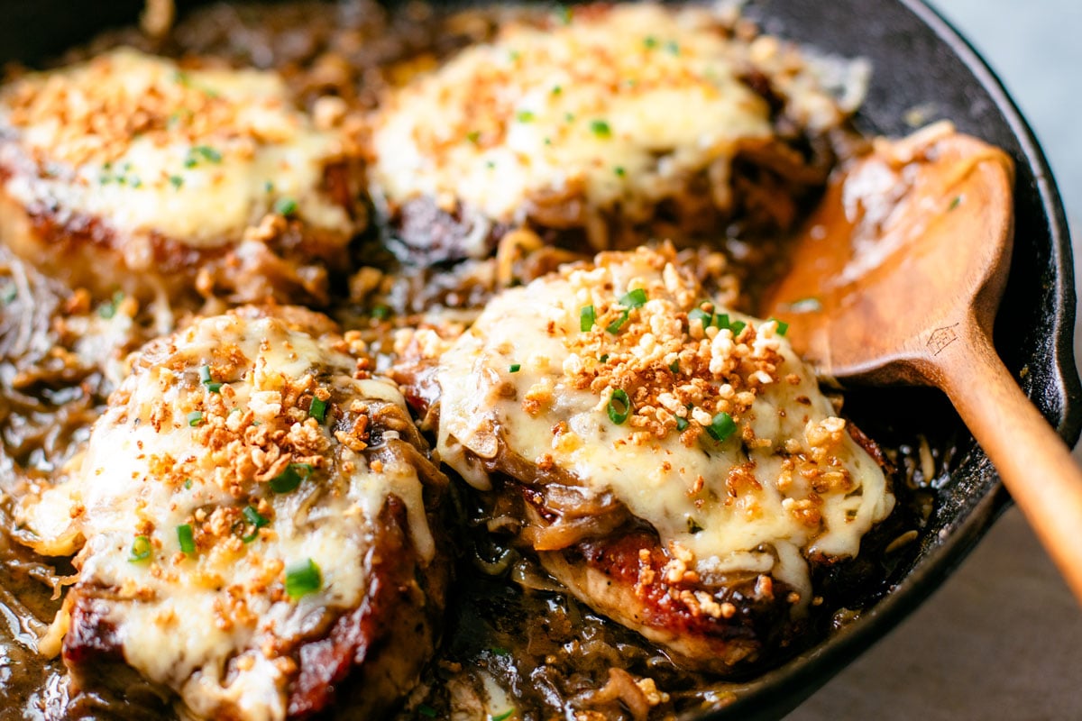 Pork chops nestled in onion gravy into a skillet.