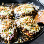 Cheesy pork chops smothered in onion gravy and topped with chives and toasted breadcrumbs in a cast iron skillet.