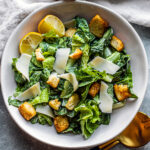 Serving bowl of Caesar salad with croutons and parmesan shavings.