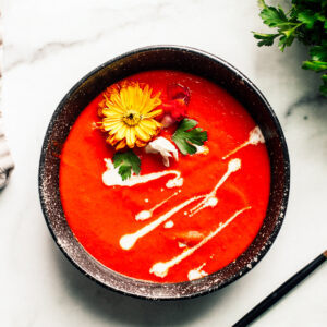 Bowl of roasted red pepper soup garnished with whirls of cream and edible flowers.