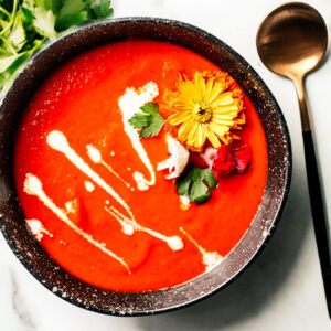 Bowl of roasted red pepper soup garnished with whirls of cream and edible flowers.