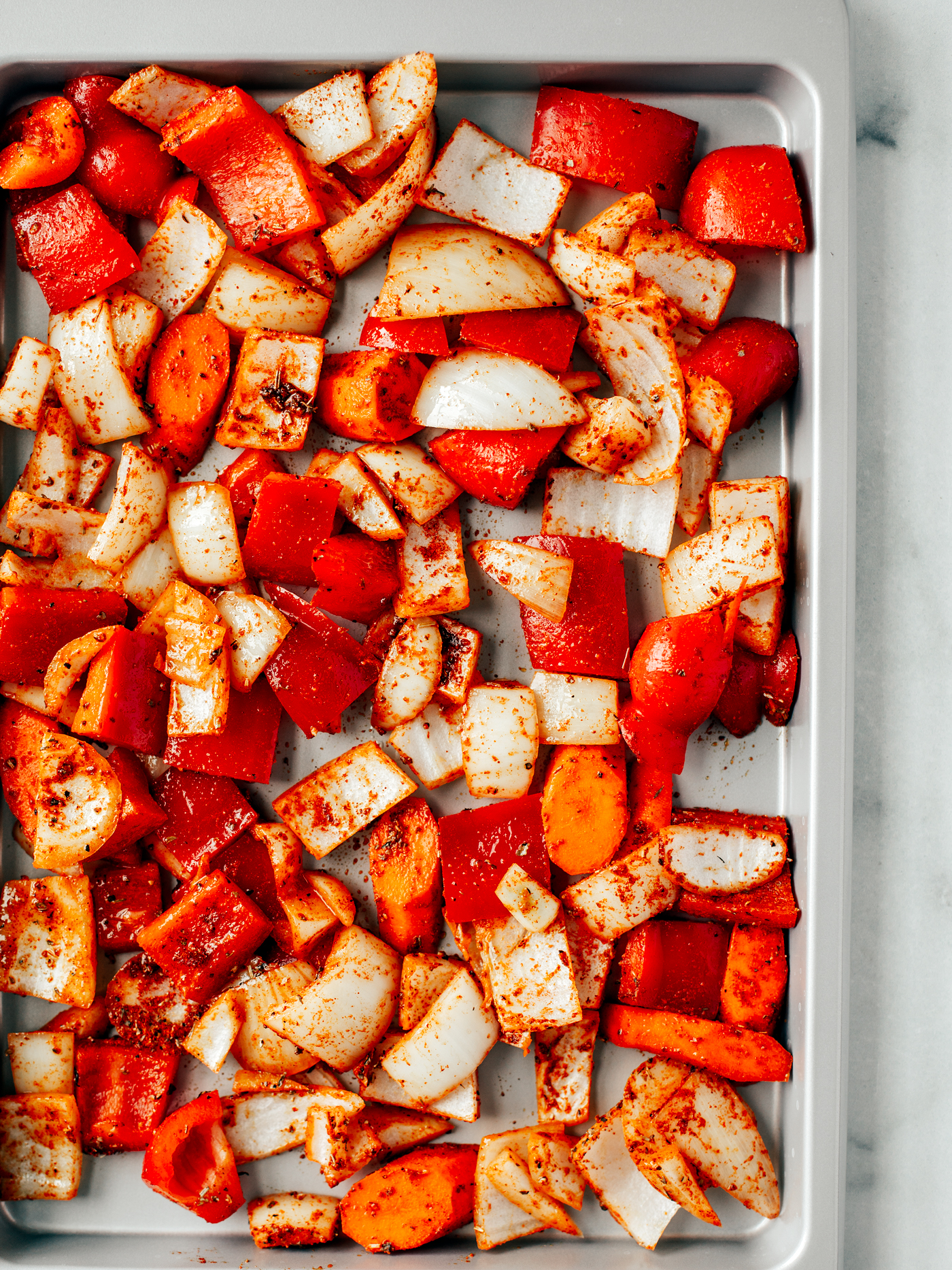 Sheet pan topped with full of chopped and seasoned peppers, onions, and carrots.